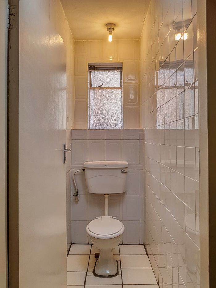 Compact white bathroom with tile walls and vintage toilet, illuminated by warm bulb light.
