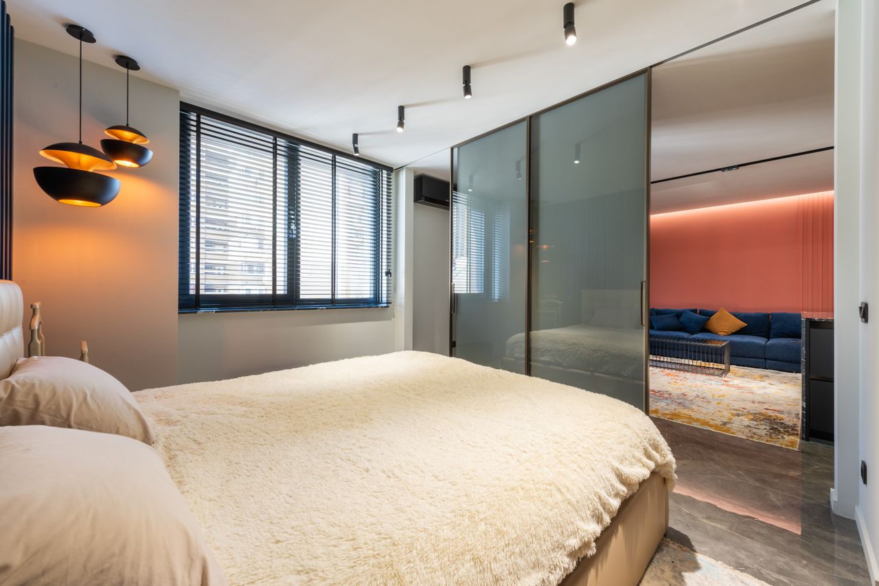 Bed with pillows and cover against glass wall and window in house with lamps in daytime